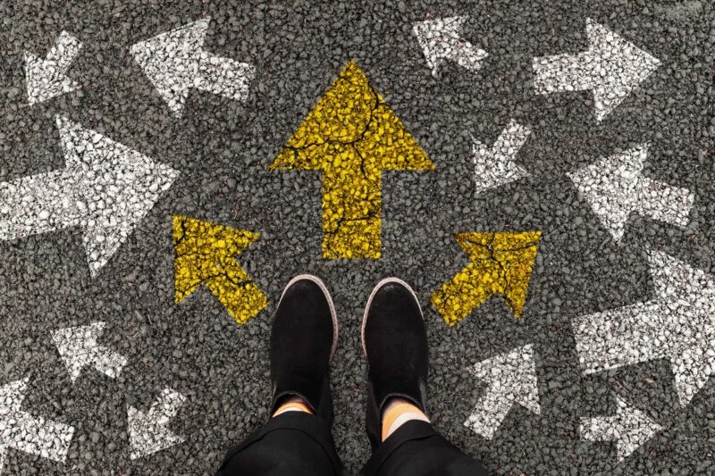 Person standing on road with arrow markings pointing in different directions or pathway, decision making concept. Top view.
