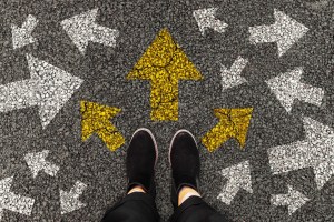 Person standing on road with arrow markings pointing in different directions or pathway, decision making concept. Top view.